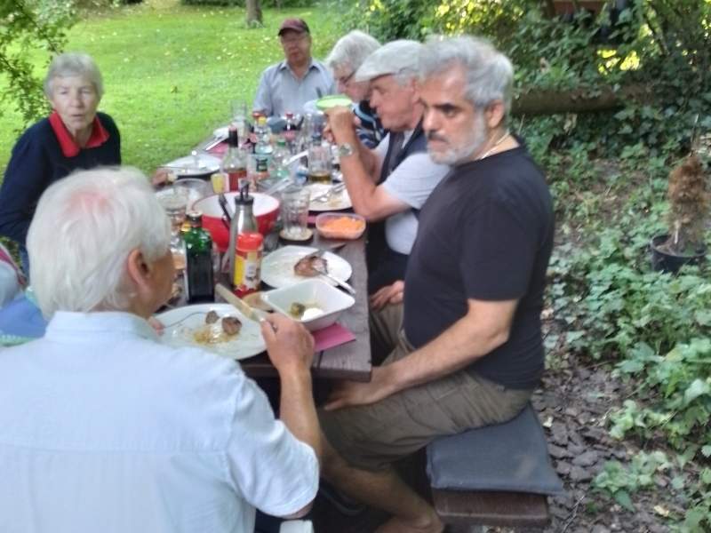 Mitglieder des Schachclubs Büsum sitzen an einem großen Tisch im Garten und essen gemeinsam.